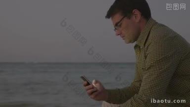 年轻的潮人风格的男人独自坐在海边，用智能手机发<strong>短信</strong>或浏览网页